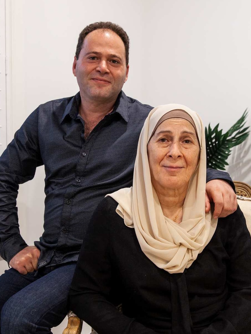 You view a middle aged man leaning against a chair, with an elderly woman in a Hijab sitting next to him.