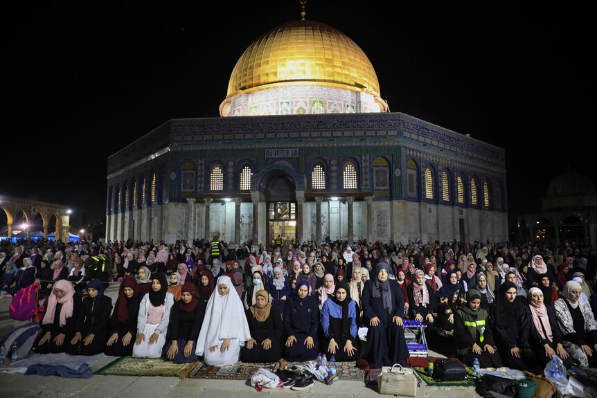 Palestinian Muslims pray in front of a gold-tipped mosque