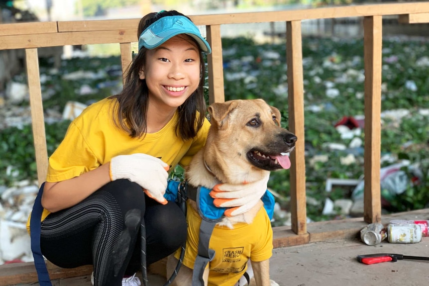 A 12-year-old girl kneels next to a dog while posing for a photo in front of a dirty canal.