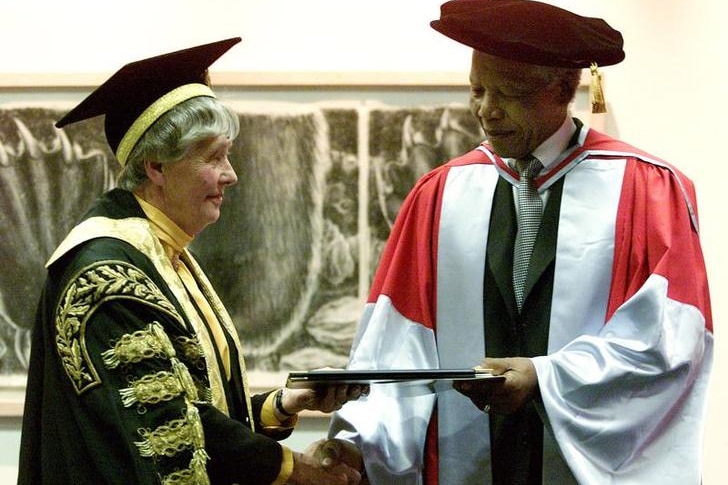 Dame Leonie Kramer, left, wears black robes with gold embellishment with Nelson Mandela, in white and silver. They shake hands.