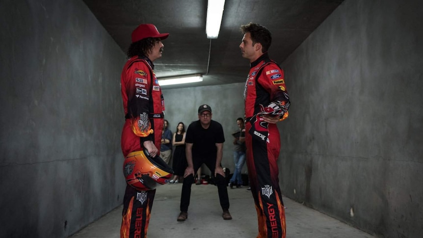 Still image of Seth MacFarlane and Sebastian Stan dressed in NASCAR attire standing in a narrow concrete corridor.