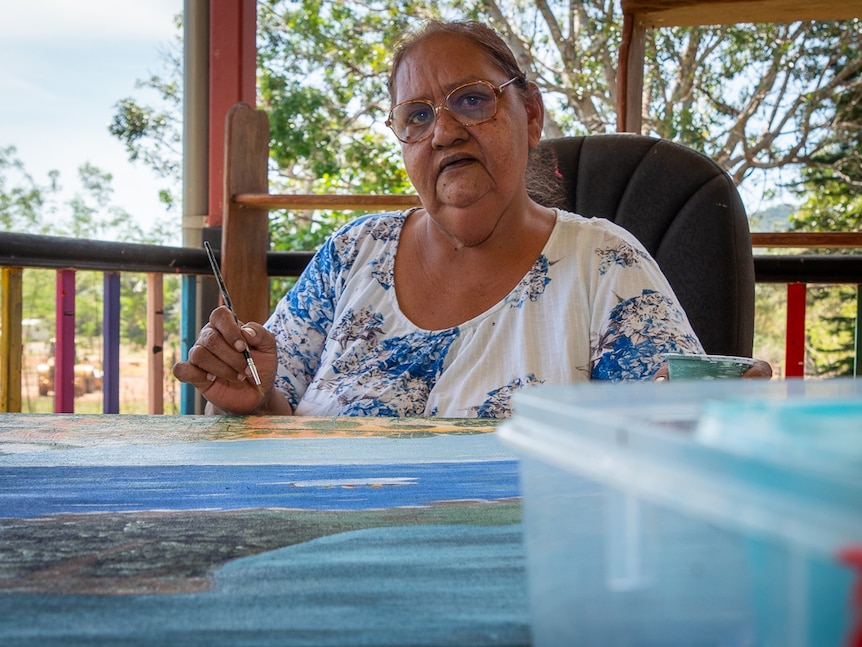Aboriginal woman painting looks at the camera