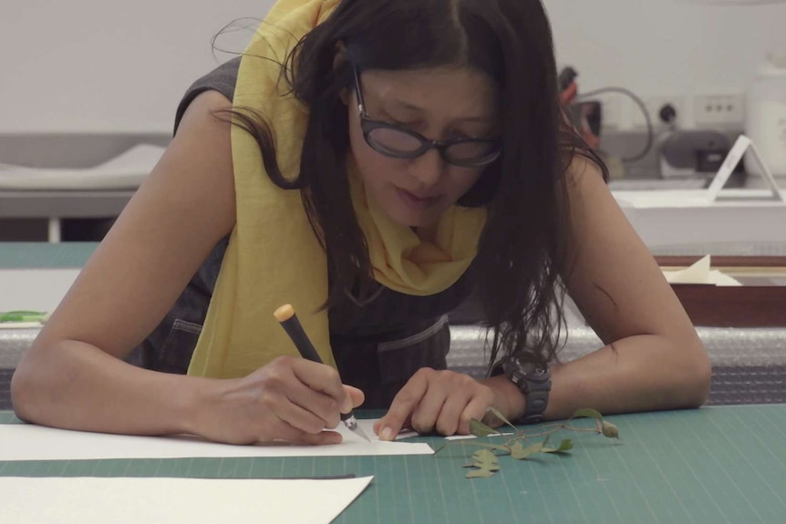 A woman cuts out paper to create a paper cut art work.