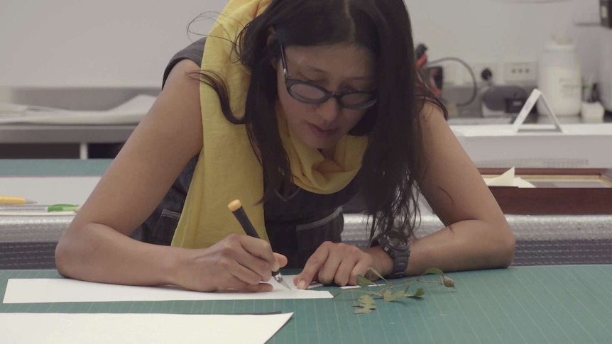 A woman cuts out paper to create a paper cut art work.