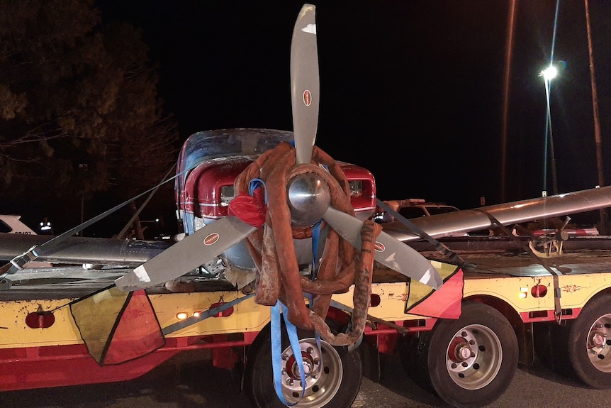 A photo of the wreckage of a red plane on the back of a truck with the propeller tied up.