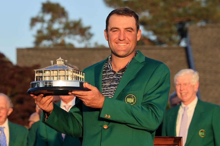 Scottie Scheffler smiles while wearing a green jacket and holding the Masters trophy
