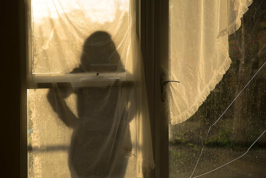A silhouette of a woman facing a window.