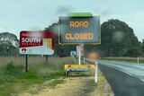 An electronic sign at the roadside reads 'road closed' stands adjacent a 'Welcome to South Australia' sign