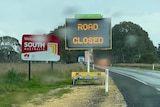 An electronic sign at the roadside reads 'road closed' stands adjacent a 'Welcome to South Australia' sign