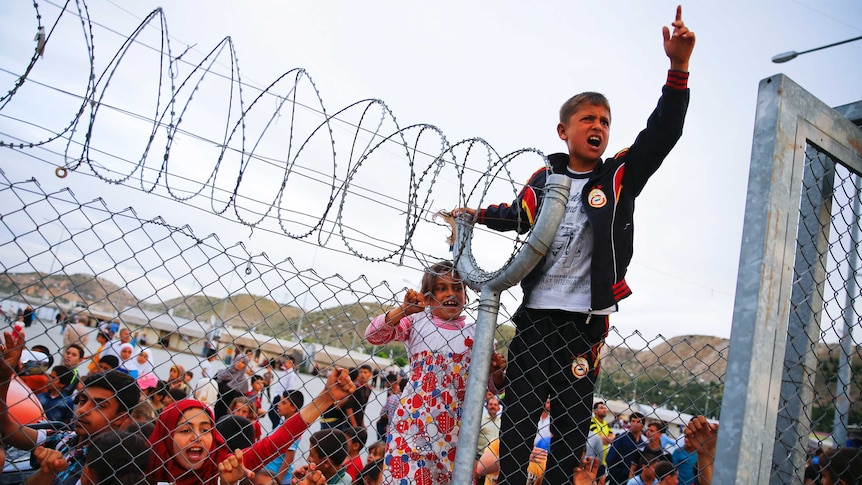 Refugee youth gestures from behind a barbed wire fence Nizip refugee camp near Gaziantep, Turkey, April 23, 2016