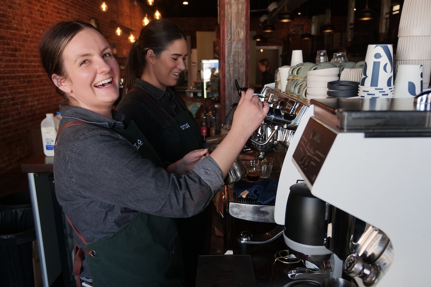 A medium shot of two workers next to the coffee machine