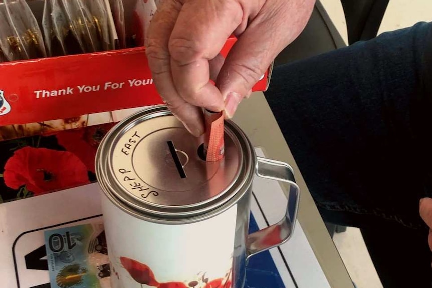 Man places a twenty dollar bill in a fundraising tin to pay for a fundraising poppy