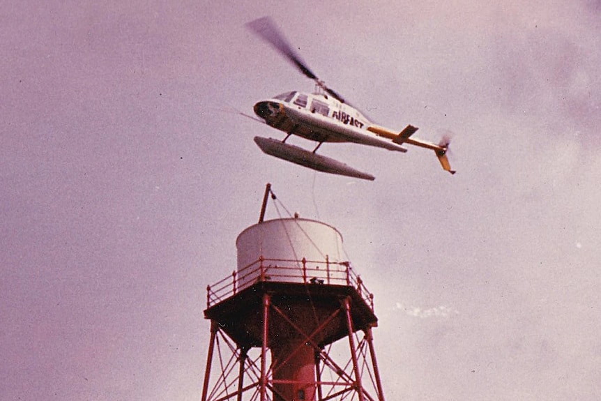 A helicopter hooves above a lighthouse.