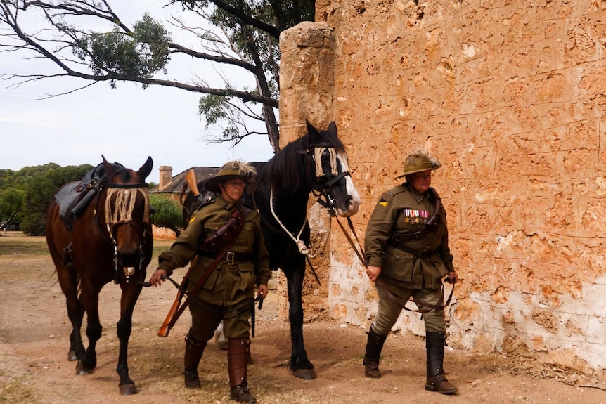 Natasha Pearce and Verna Holmes leading their horses through historic buildings in Greenough, dressed in World War I attire.