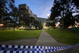 At dusk, you look up to a y-shaped brutalist public housing tower while police tape is in the foreground.