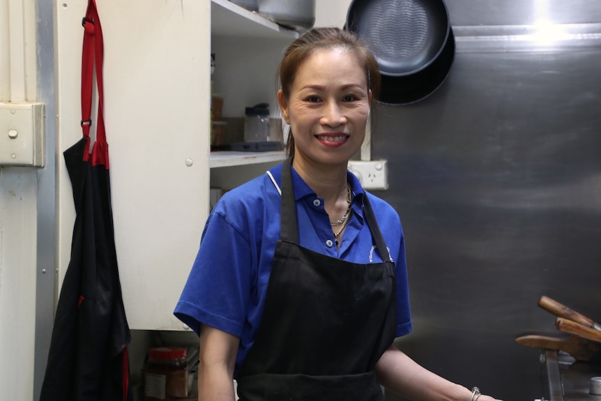 A Vietnamese woman in an apron in a commercial kitchen with a big smile on her face.