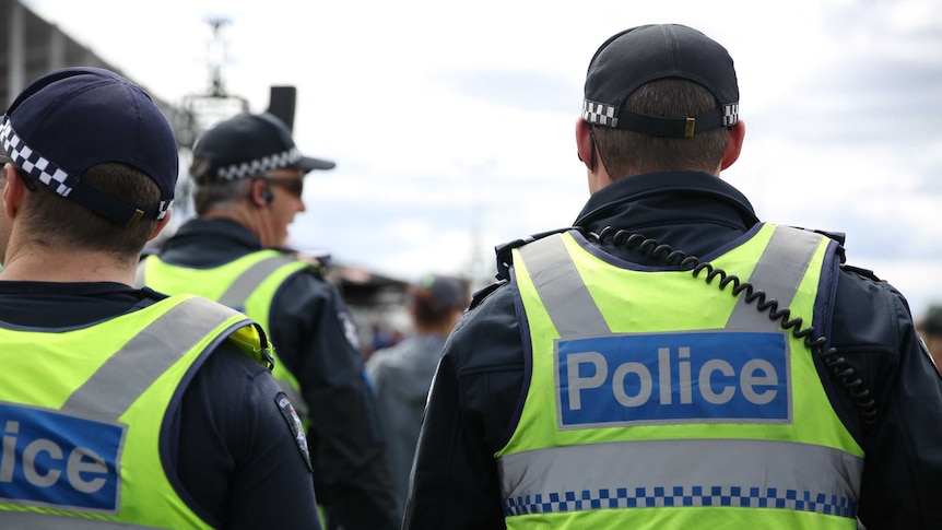 Three Victoria Police officers in uniform, pictured from behind.