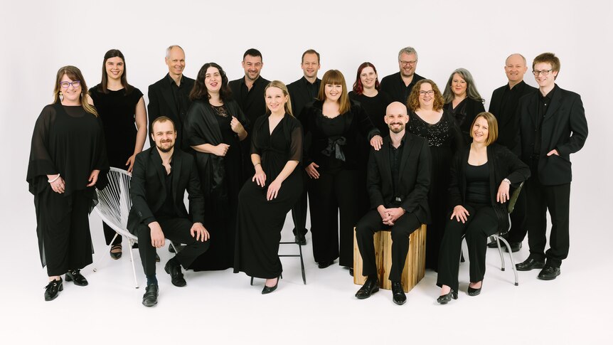 The Adelaide Chamber Singers dressed in black, posed in front of an all-white background.