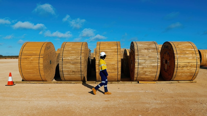 A person in high-vis clothes walks past large barrels in the outback.