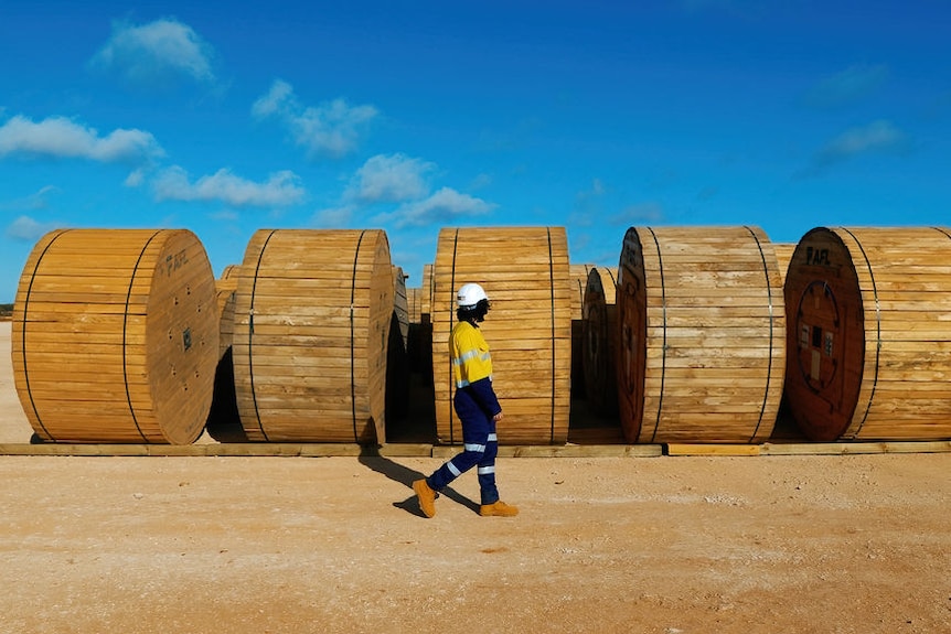 A person in high-vis clothes walks past large barrels in the outback.