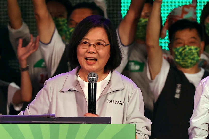 Tsai Ing-wen holding a microphone and wearing a jacket speaks in front of supporters
