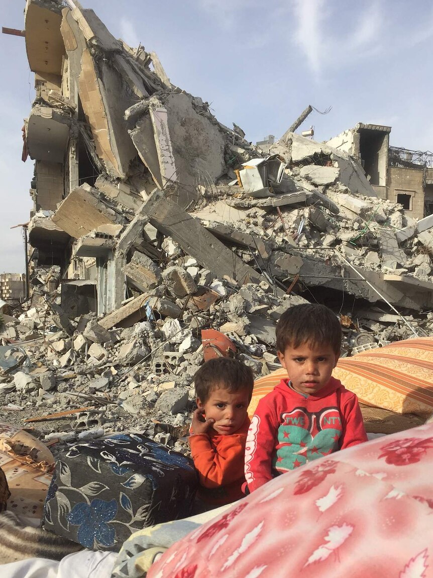 The children of Ahmed Hussein sit with all they own in front of their destroyed apartment block.