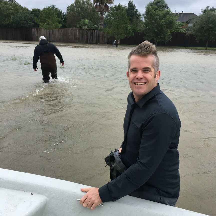 Conor Duffy holding onto dinghy while standing in floodwaters and man in background wades through water.