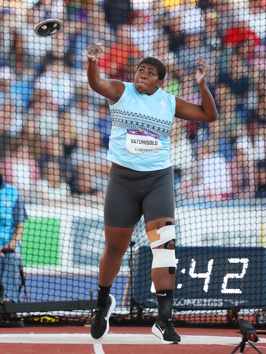 A woman wearing blue and black throws a discus during an event