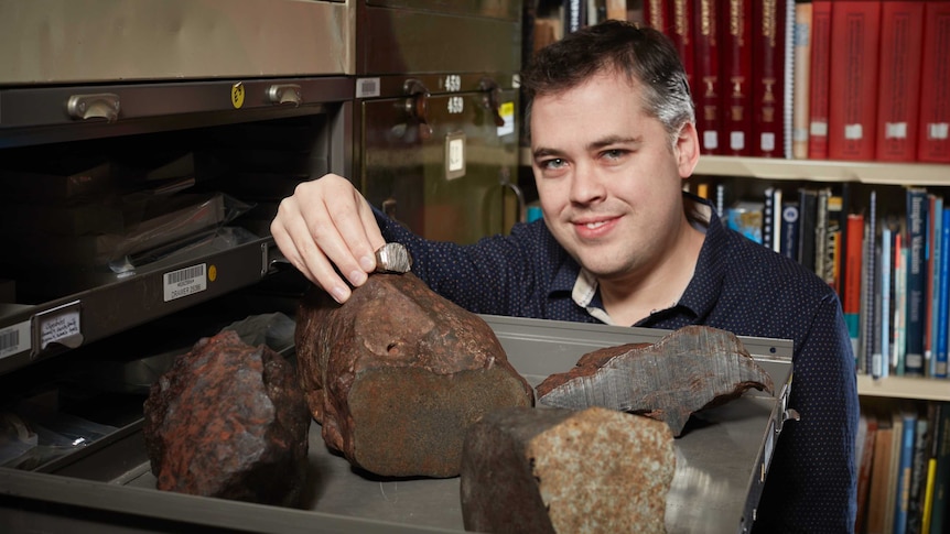 A man standing in front a filing cabinet full of rocks