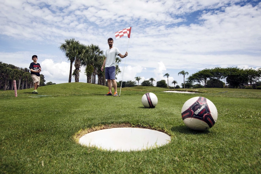 Patrick Wooten (C) holds the flag as his son Thomas (L) misses a putt at FootGolf course in Florida.