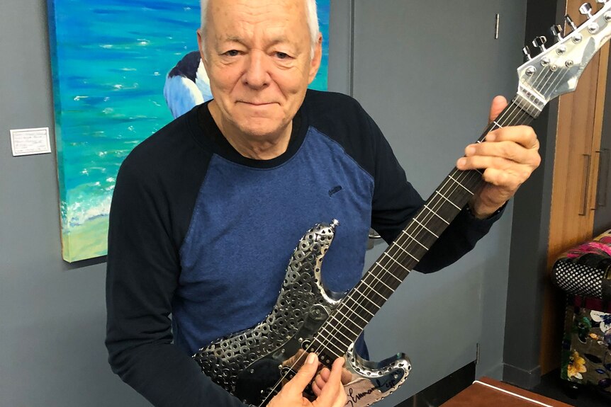 Tommy Emmanuelle sits down holding a shiny silver metal guitar.