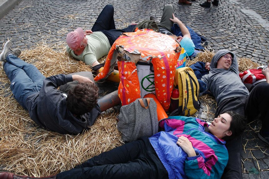 A group of people lie on hay on the cobbled path in France with a banner or object between them.