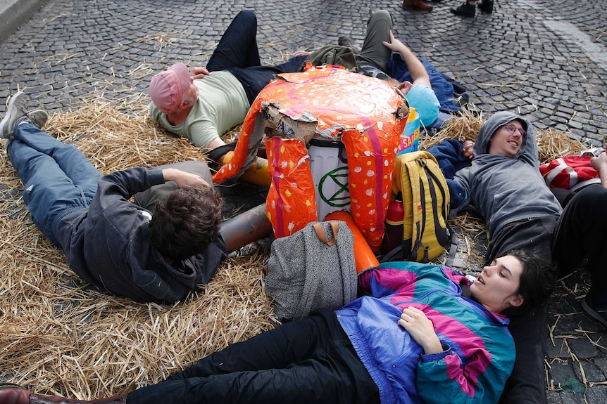 A group of people lie on hay on the cobbled path in France with a banner or object between them.