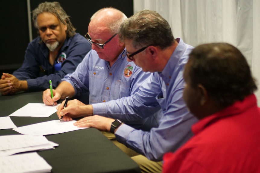 Four men sign an agreement at a desk