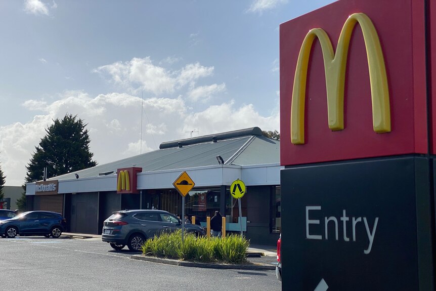 A sign with a McDonald's logo in the foreground and a building in the background. 