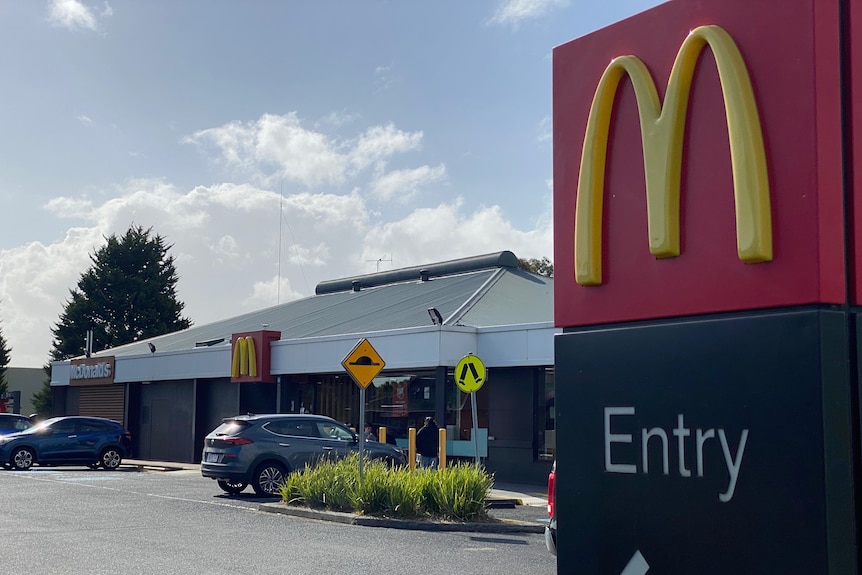 A sign with a McDonald's logo in the foreground and a building in the background. 