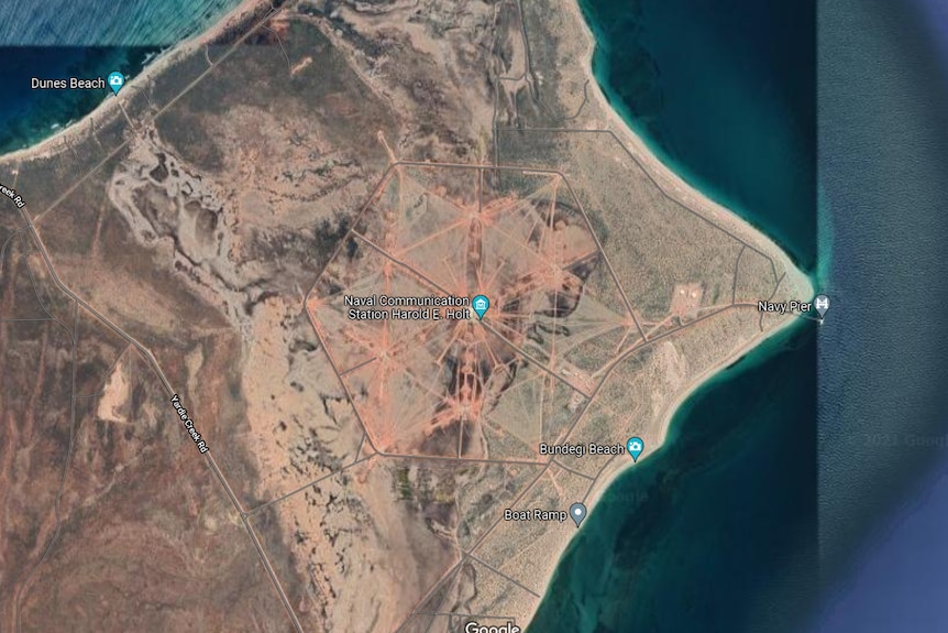 An aerial satellite shot over a desert area by a coast with a hexagon road around a compound in the middle