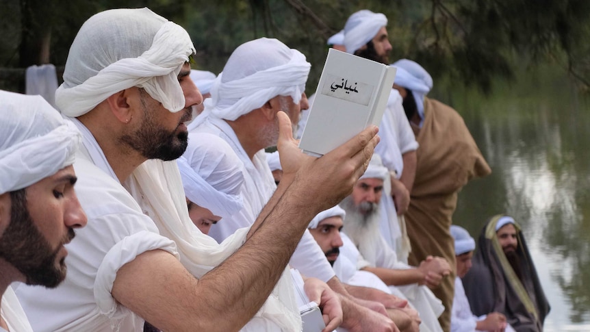 Profile shot of robed men in line praying and reading Mandaean scripture.