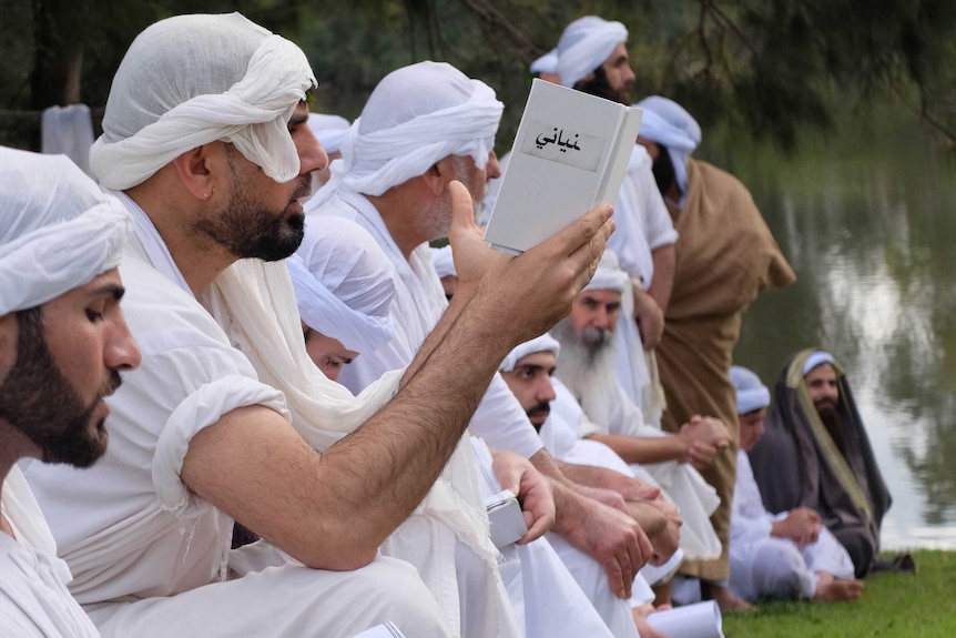Profile shot of robed men in line praying and reading Mandaean scripture.