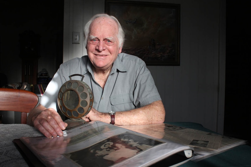 Portrait of an older man with grey hair and bright blue eyes sitting at a desk with an old radio microphone