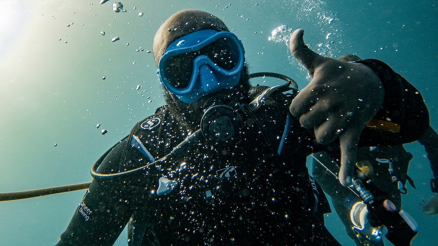 A scuba diver takes a selfie underwater. 