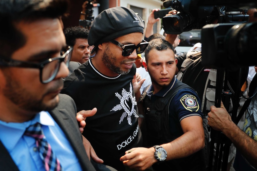Ronaldinho leaves the attorney general's office surrounded by cameras.