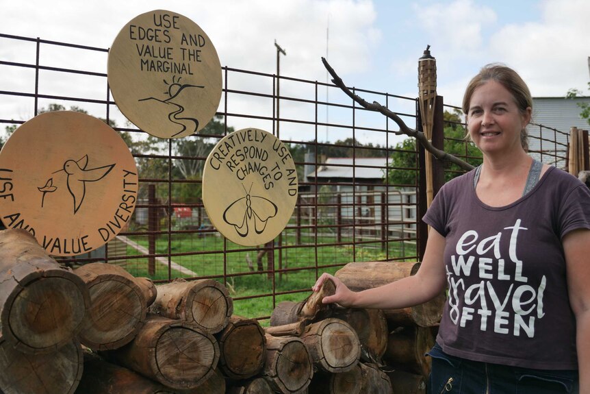 A woman standing near signs that have environmental messages near a load of wood logs