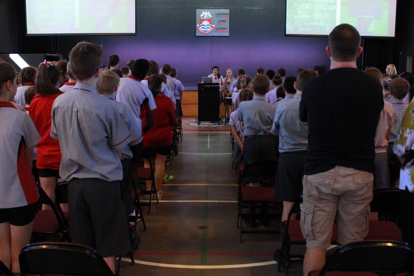 students and teachers stand at assembly