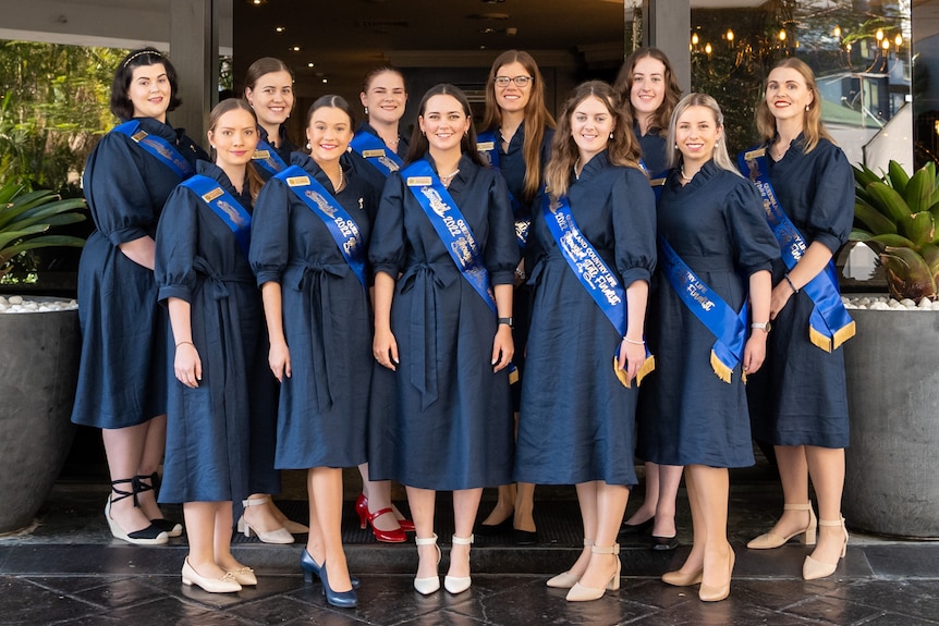 A group of young women in the same dresses and sashes smiling
