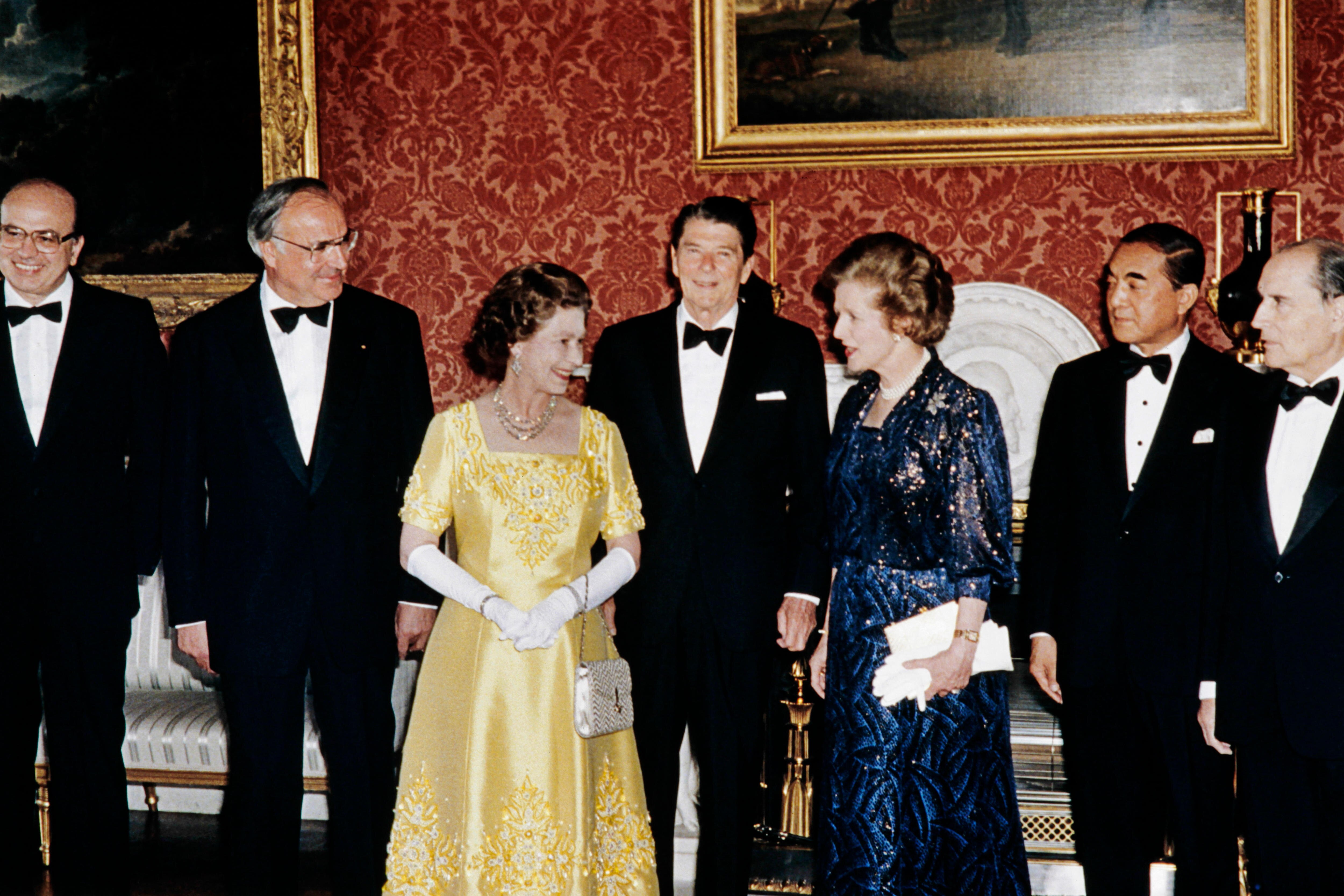 Queen Elizabeth II and Margaret Thatcher face each other in a room full of men.