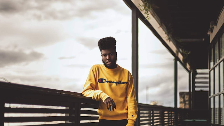 image of khalid standing on a balcony leaning against the railing dressed in yellow