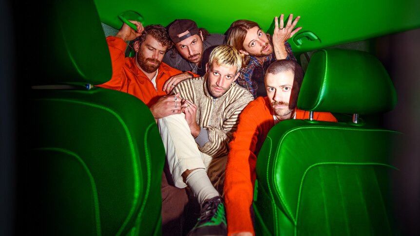 Five men, two in orange jackets, sit in the back seat of a car with bright lime green interiors