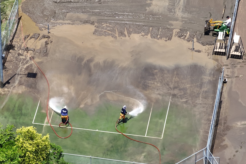An aerial shot of two crews hosing down a muddy tennis court.