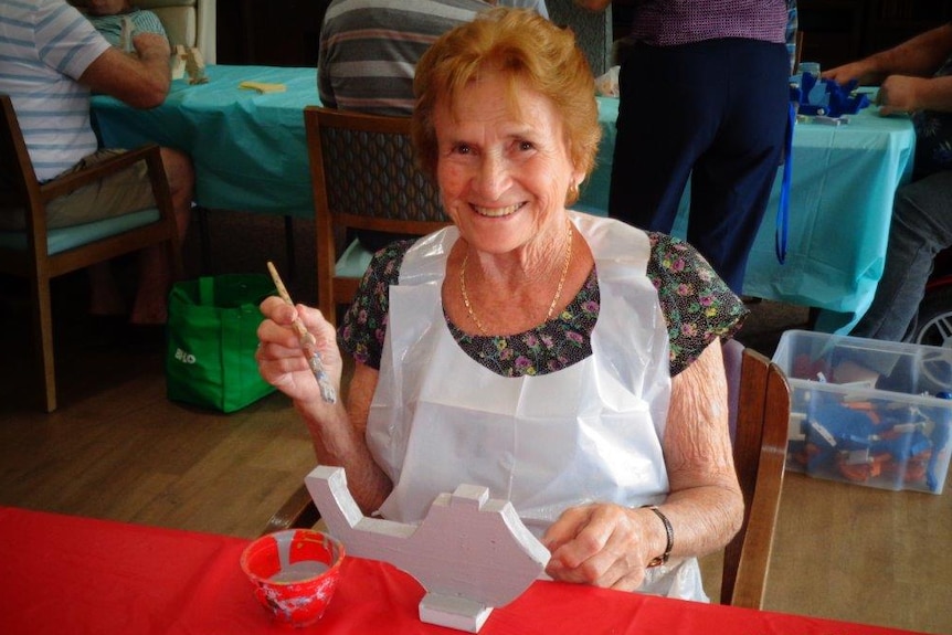 Photograph of elderly woman painting a wooden toy helicopter.